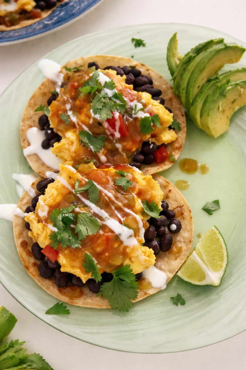 Breakfast tostadas with scrambled egg, black beans, salsa, crema and cilantro, with avocado and lime