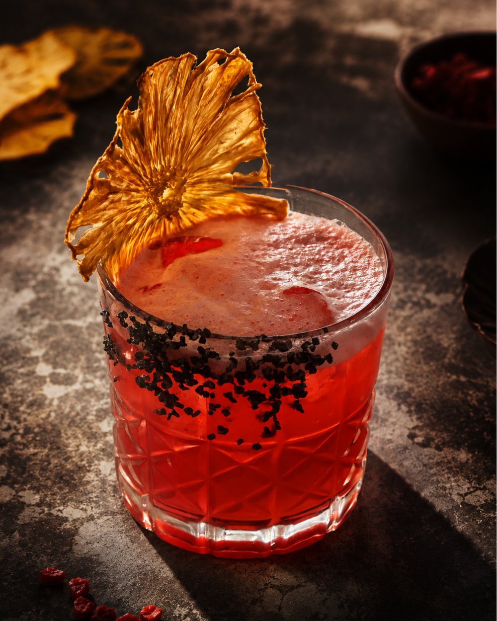 A Hibiscus Haze cocktail with a black salt rim and a dehydrated pineapple flower