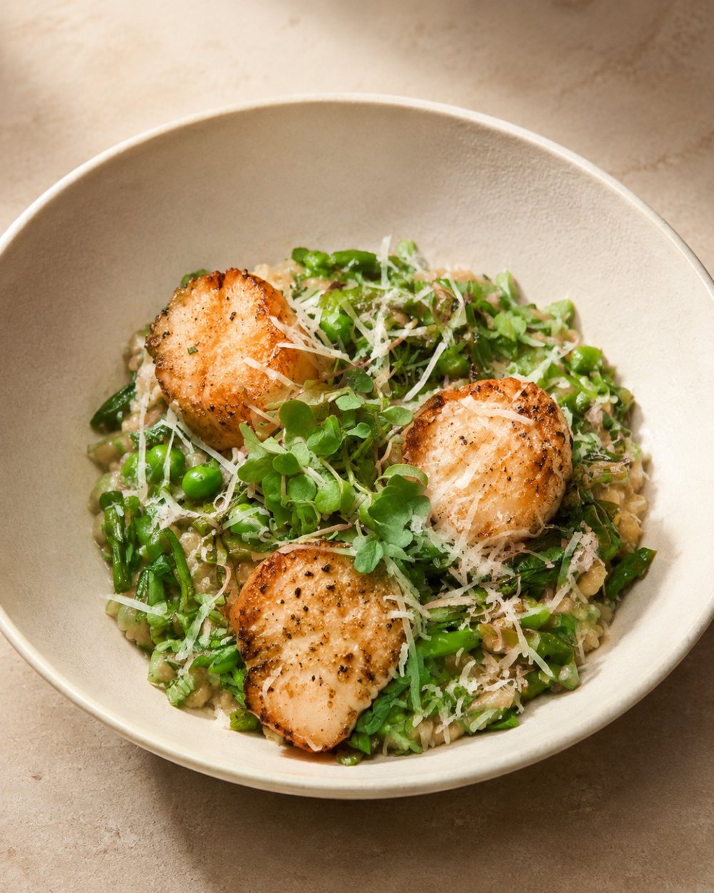 Spring risotto with peas and seared scallops in a shallow white bowl